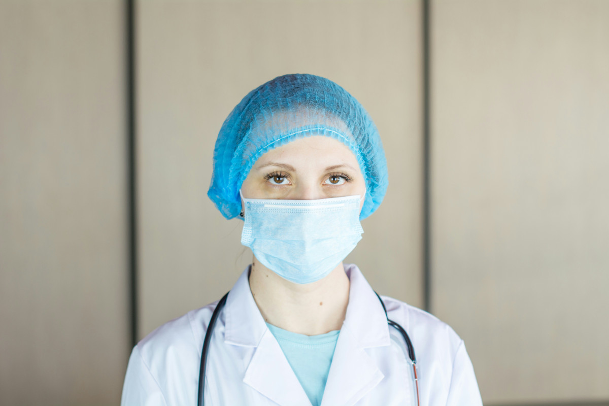 Photo d’un médecin. Elle porte un masque médical bleu obsolète, une casquette bleue et une blouse blanche. Photo : Bermix Studio / Unsplash.